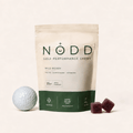 A stand-up pouch of NODD Golf Performance Chews in Wild Berry flavor, shown on a light beige background with a golf ball and two dark berry chew cubes.